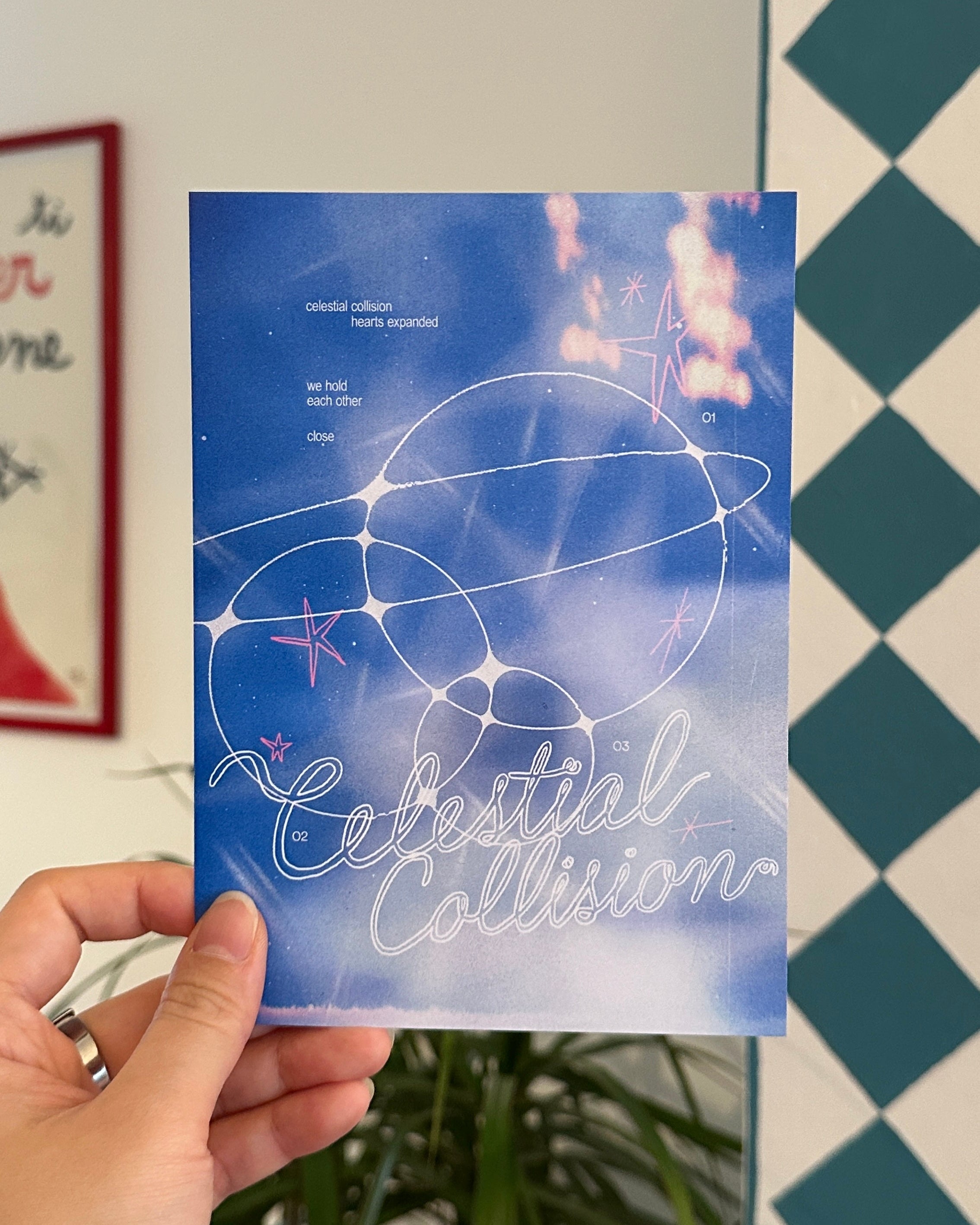 Hand holding a blue card with 'Celestial Collision' text against a checkered wall.