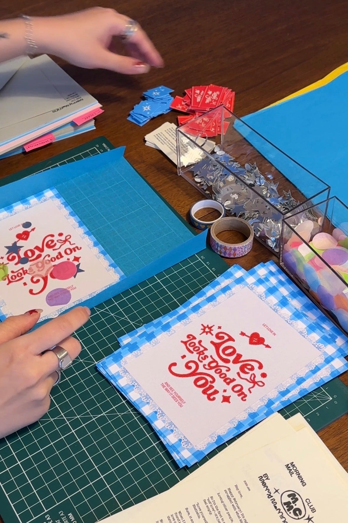 Hands working on a craft project with printed materials and stationery items on a table.